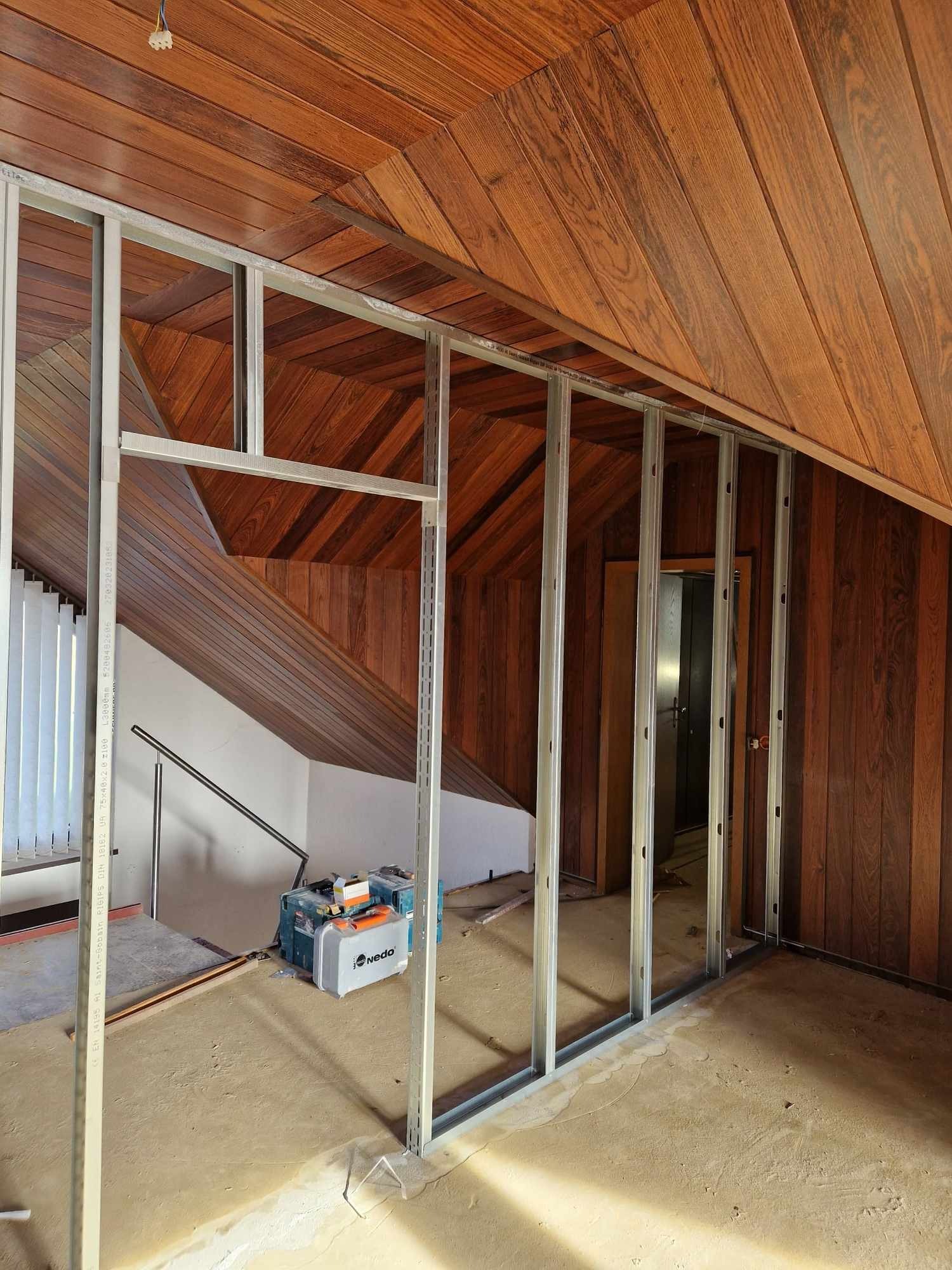 Konstrukcja z metalowych profili na poddaszu z boazerią, widoczne narzędzia i skrzynka Nedo, przygotowanie do montażu płyt kartonowo-gipsowych.
