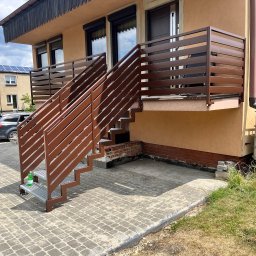 Dan-Technnik Daniel Hoszek - Brązowe schody metalowe z balustradą prowadzące na balkon domu. Widoczne poziome elementy balustrady i metalowe stopnie. Na pierwszym planie butelka wody.