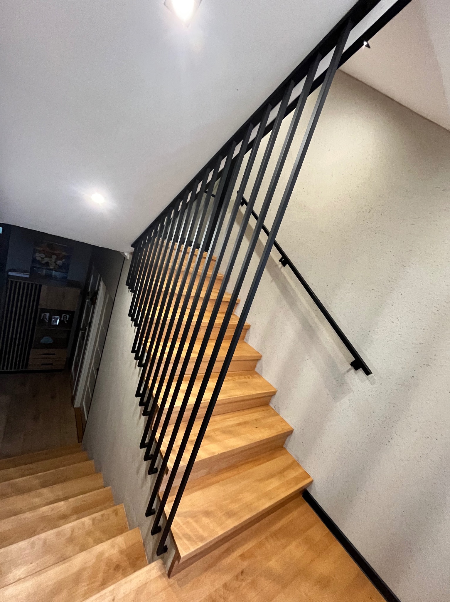 Nowoczesne schody drewniane z czarną, minimalistyczną balustradą metalową. Ujęcie z dołu, podkreślające geometrię i kontrast materiałów.