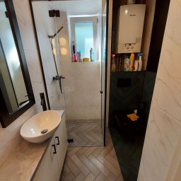 GRUPA FACHOWO SPÓŁKA Z OGRANICZONĄ ODPOWIEDZIALNOŚCIĄ - Nowoczesna łazienka z kabiną prysznicową typu walk-in, umywalką nablatową i wiszącym sedesem. Ściany wyłożone płytkami imitującymi marmur, podłoga w jodełkę. Na ścianie nad sedesem zamontowany piec...