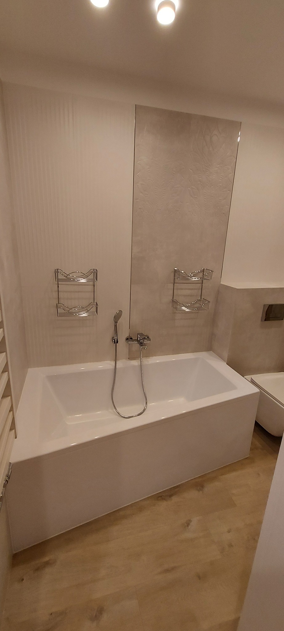 Nowoczesna, biała wanna w łazience z beżowymi płytkami, chromowaną armaturą i półkami na kosmetyki.