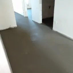 Świeżo wylana, gładka posadzka w jasnym wnętrzu z białymi ścianami i widocznymi puszkami elektrycznymi, perspektywa z niskiego kąta.