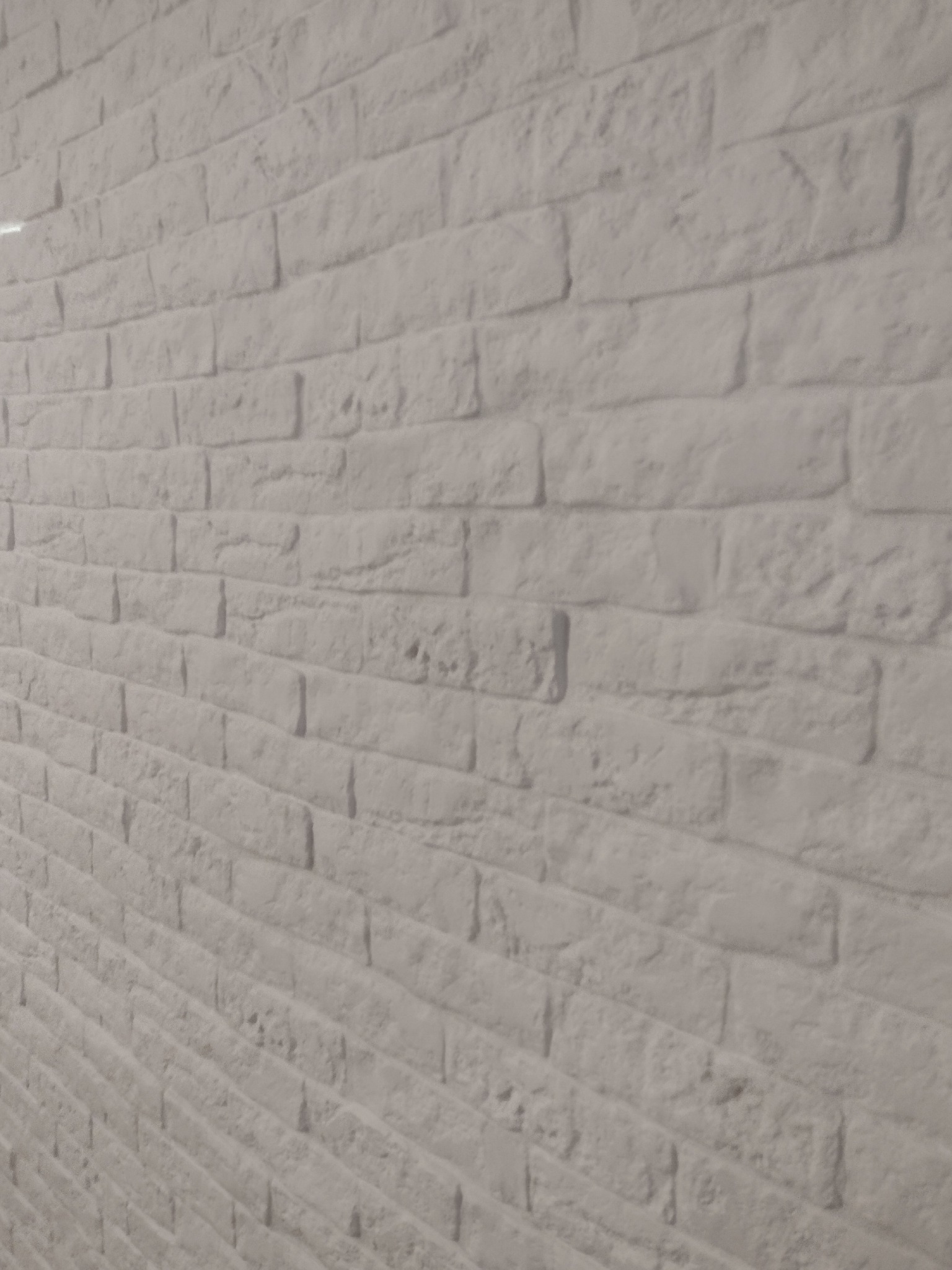 Ściana z białej cegły dekoracyjnej, ułożona pod kątem, z widoczną fakturą i nierównościami, oświetlona z lewej strony.