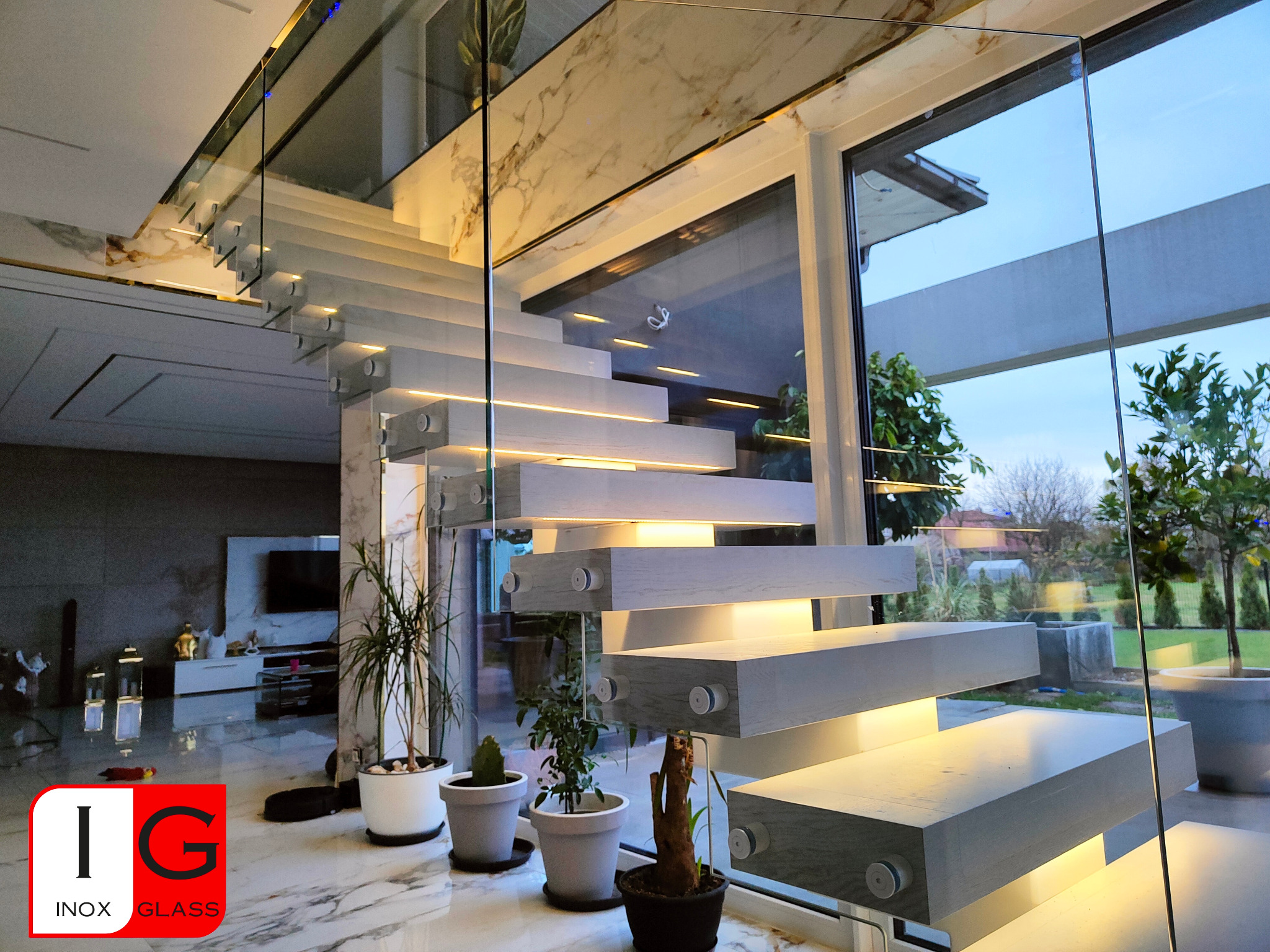 Nowoczesne, podświetlane schody z drewnianymi stopniami i szklaną balustradą w luksusowym wnętrzu z marmurową podłogą i widokiem na ogród przez duże okno.