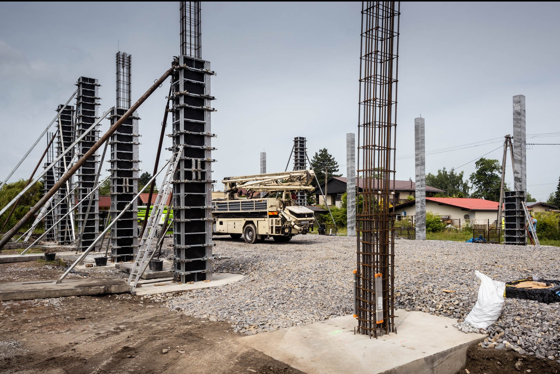 Wznoszenie żelbetowych słupów na placu budowy domu jednorodzinnego, widoczny betonowóz z pompą do betonu, szalunki, zbrojenia i gruz.