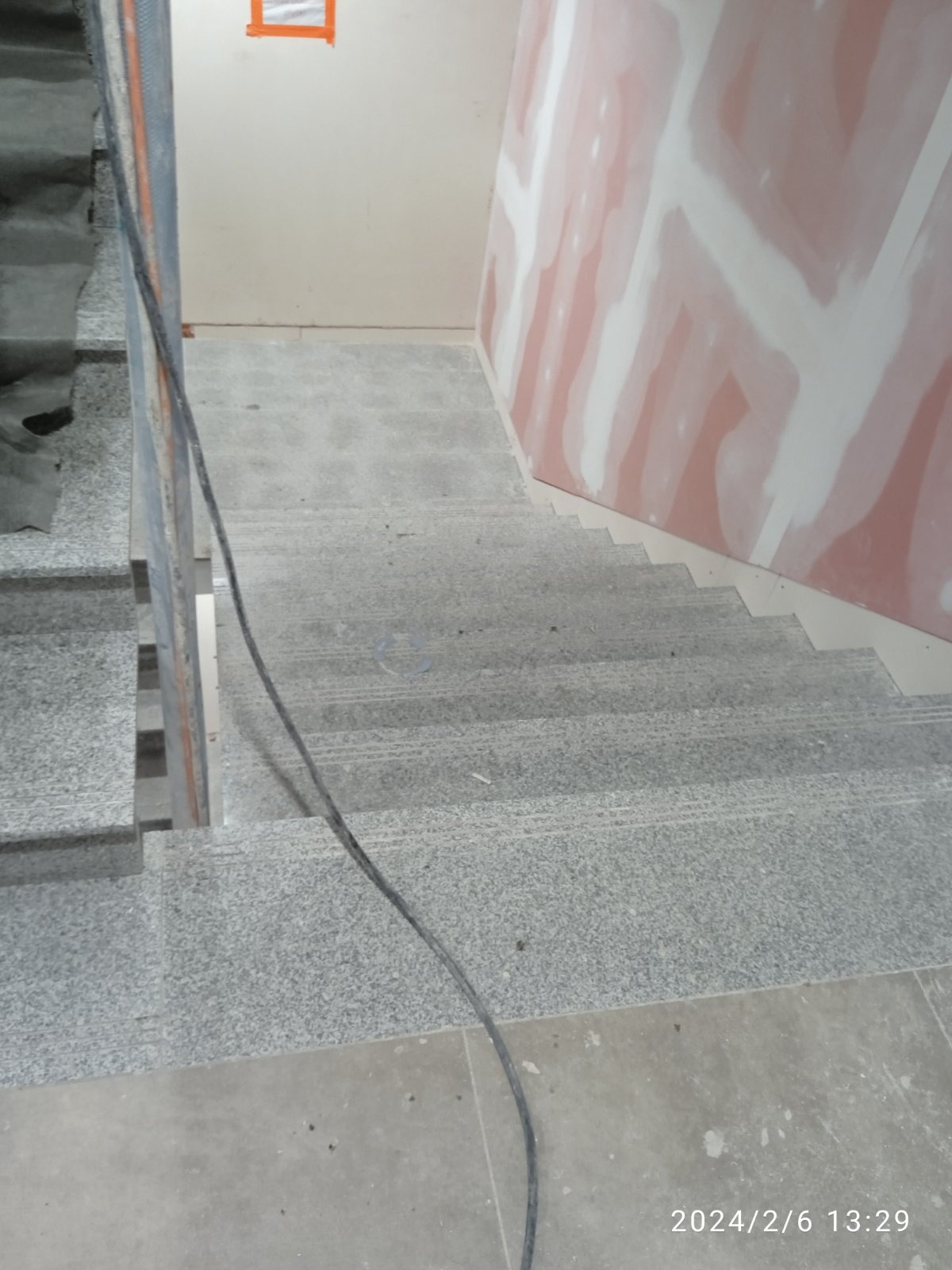 Klatka schodowa w trakcie remontu: ściany pokryte gładzią szpachlową, schody z lastryko, widoczny kabel elektryczny.