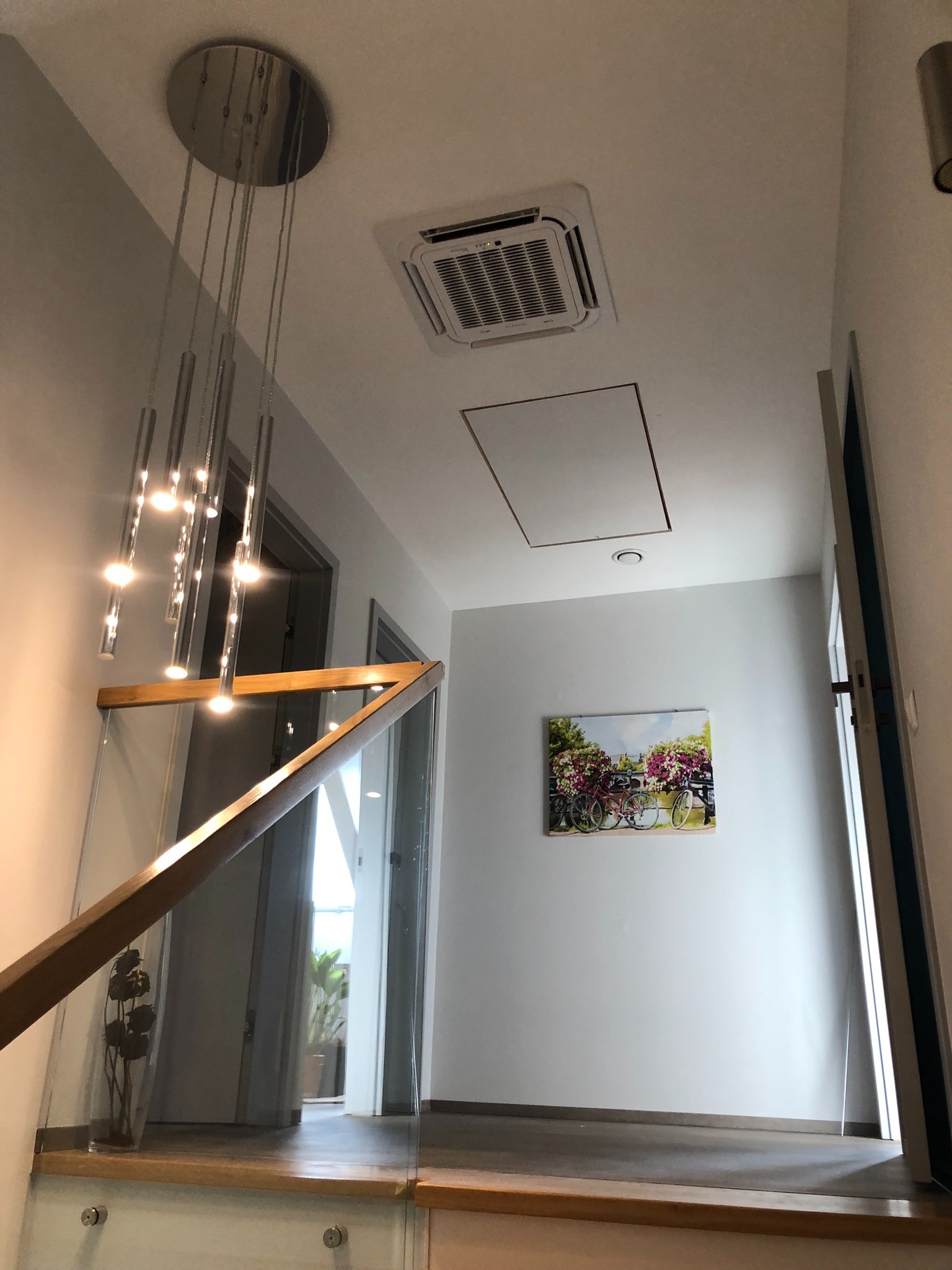 Kasetonowa klimatyzacja sufitowa zamontowana w korytarzu domu, widoczna z perspektywy schodów z szklaną balustradą i nowoczesnym oświetleniem.