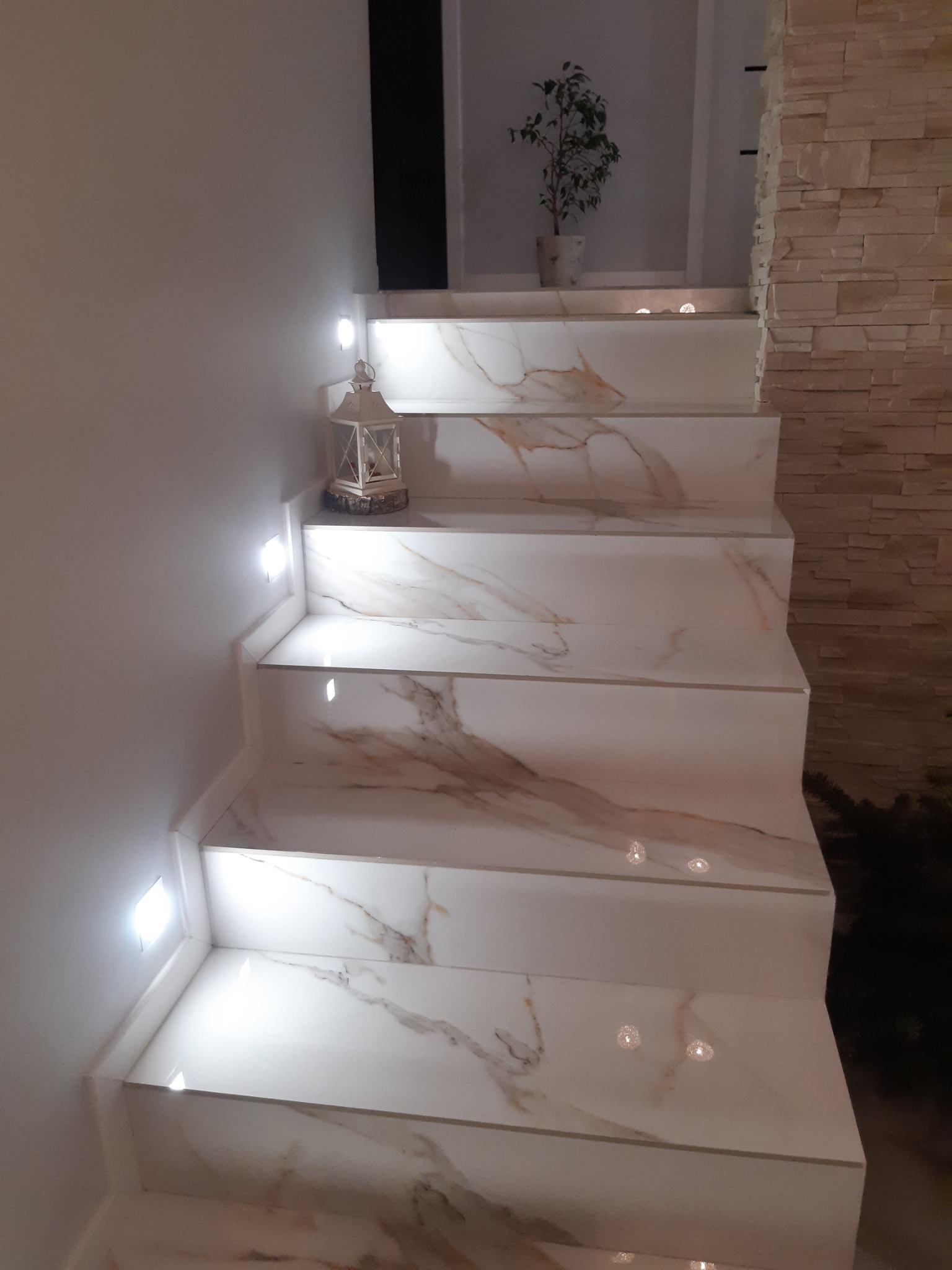 Schody wykończone białym marmurem z brązowymi żyłkami w domu w Kazimierzu Dolnym, podświetlone małymi kwadratowymi lampkami, z dekoracyjnym lampionem na jednym ze stopni.
