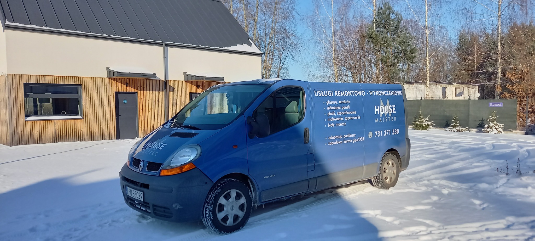 Niebieski samochód dostawczy firmy remontowo-wykończeniowej House Majster zaparkowany na śniegu przed budynkiem z drewnianą elewacją i szarą stolarką okienną i drzwiową.