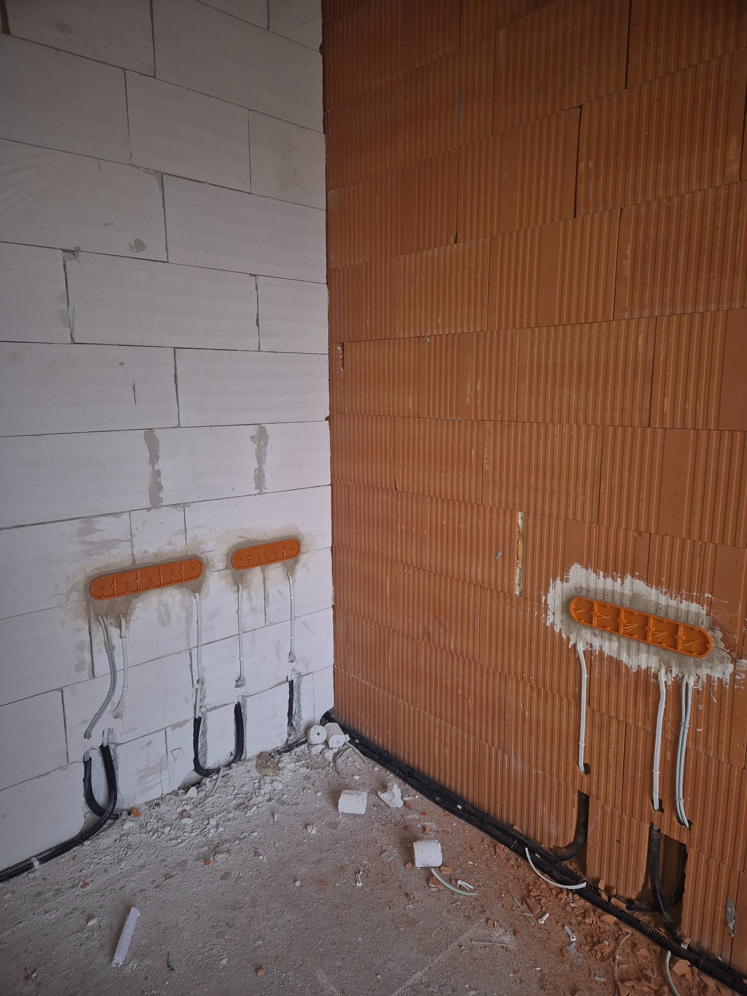 Ściana z pustaków z zamontowanymi puszkami elektrycznymi i przewodami. Widoczne kable w peszlach i przewody wychodzące z puszek. Surowy stan, przygotowanie do dalszych prac.