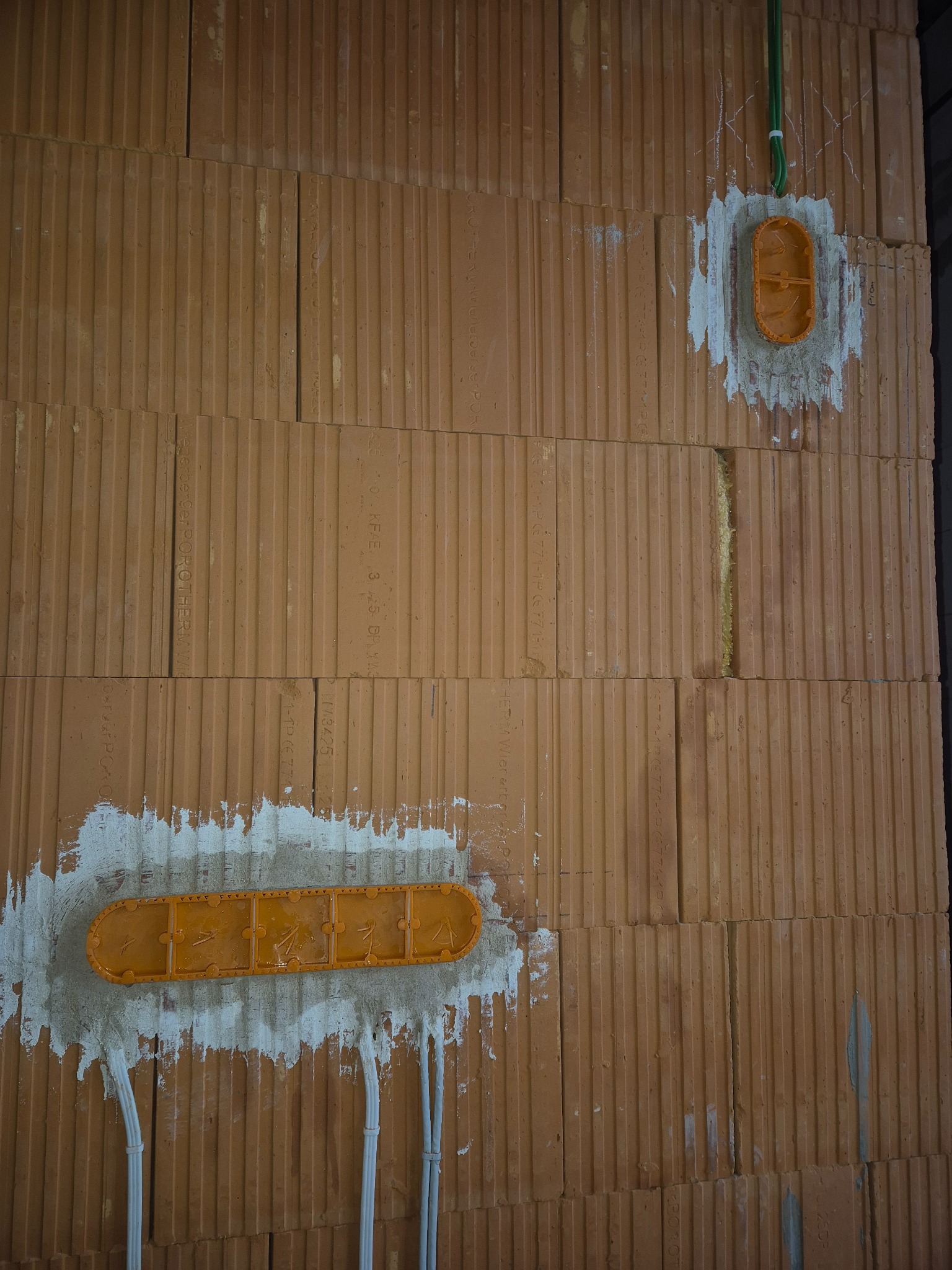 Montaż podtynkowych puszek elektrycznych w ścianie z cegły ceramicznej, widoczne przewody. Etap prac instalacyjnych przed tynkowaniem.