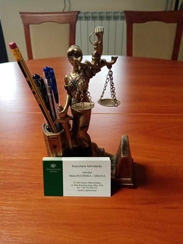 Statuetka Temidy, wizytówka kancelarii adwokackiej Marty Rucińskiej-Ojdany, ołówki i długopisy w ozdobnym pojemniku na biurku.