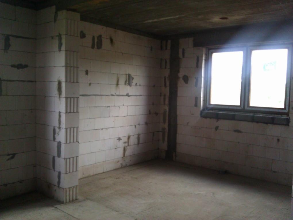 Wnętrze surowego domu w trakcie budowy, ściany z białych bloczków, widoczne okno i betonowa podłoga.