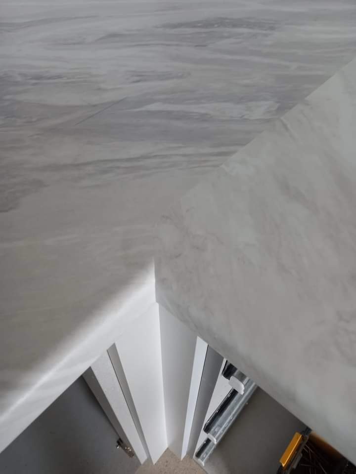 Fragment blatu kuchennego z efektem marmuru w jasnych odcieniach szarości, zamontowanego w Blachowni, widoczny z góry, z elementami montażowymi i białymi listwami przypodłogowymi.