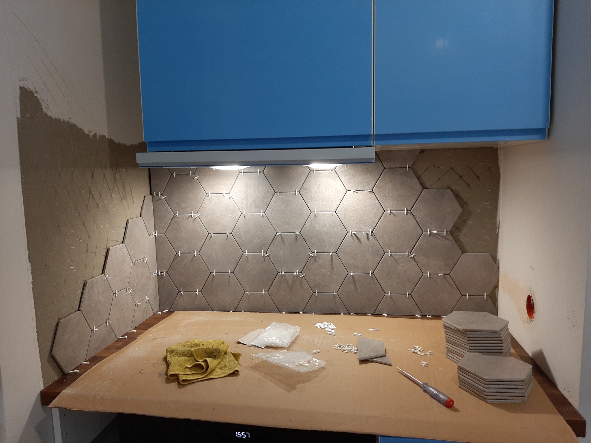 Montaż heksagonalnych płytek ceramicznych na ścianie między szafkami kuchennymi, widoczne krzyżyki dystansowe, zapas płytek, ślady zaprawy i narzędzia.