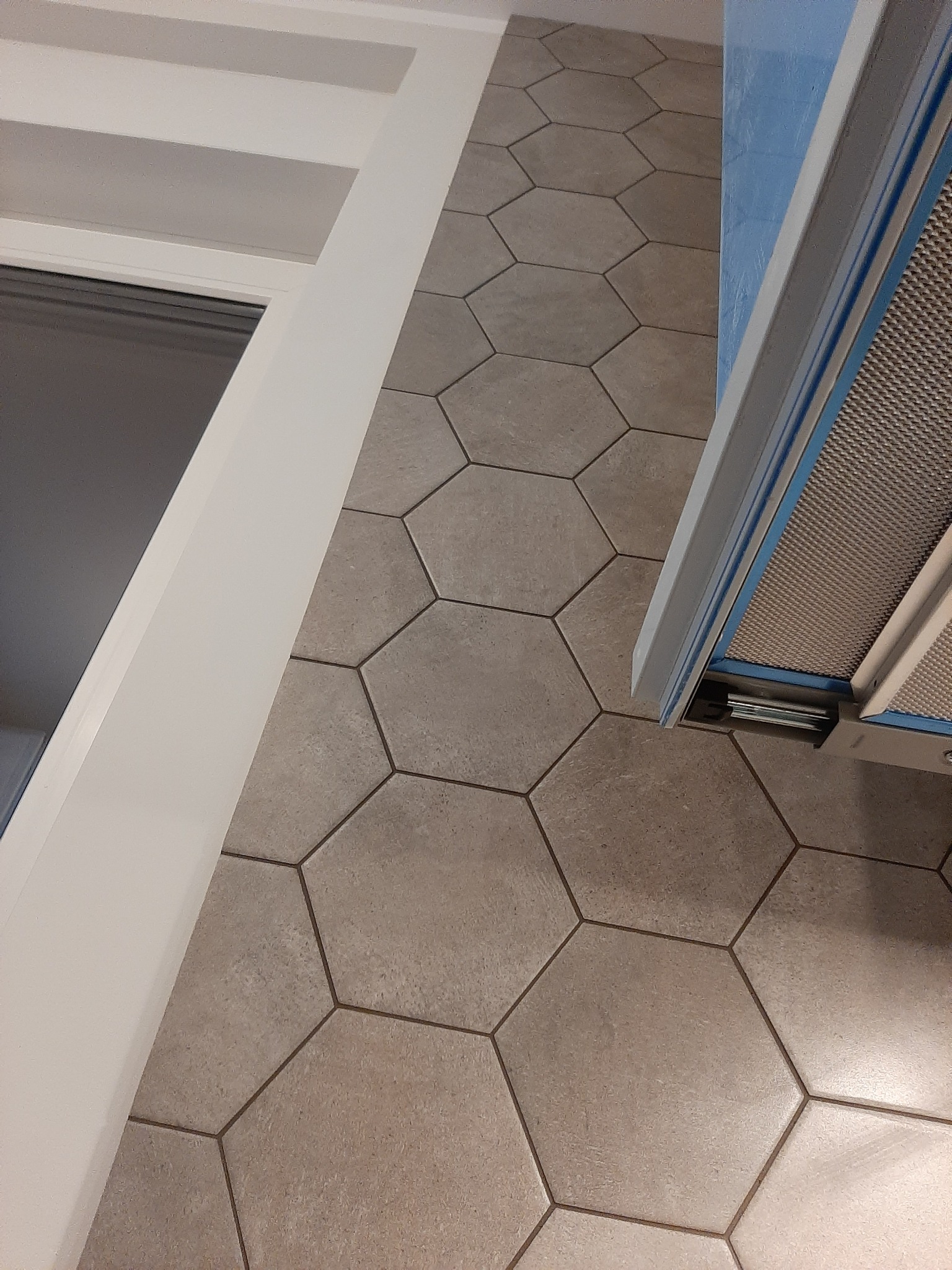Fragment wykończonej kuchni z heksagonalną terakotą na podłodze, białą listwą przypodłogową i fragmentem niebieskiej szafki z okapem.