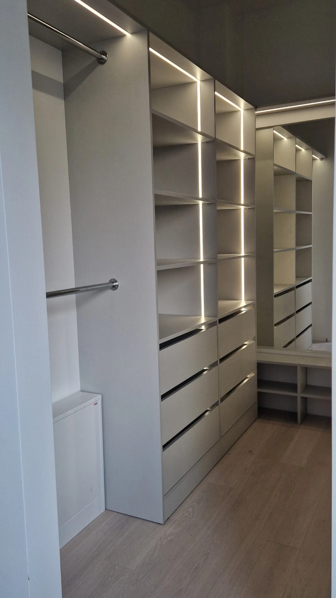 Jasna, nowoczesna garderoba z szufladami i półkami, oświetlona pionowymi paskami LED, widoczna w Stegnie.
