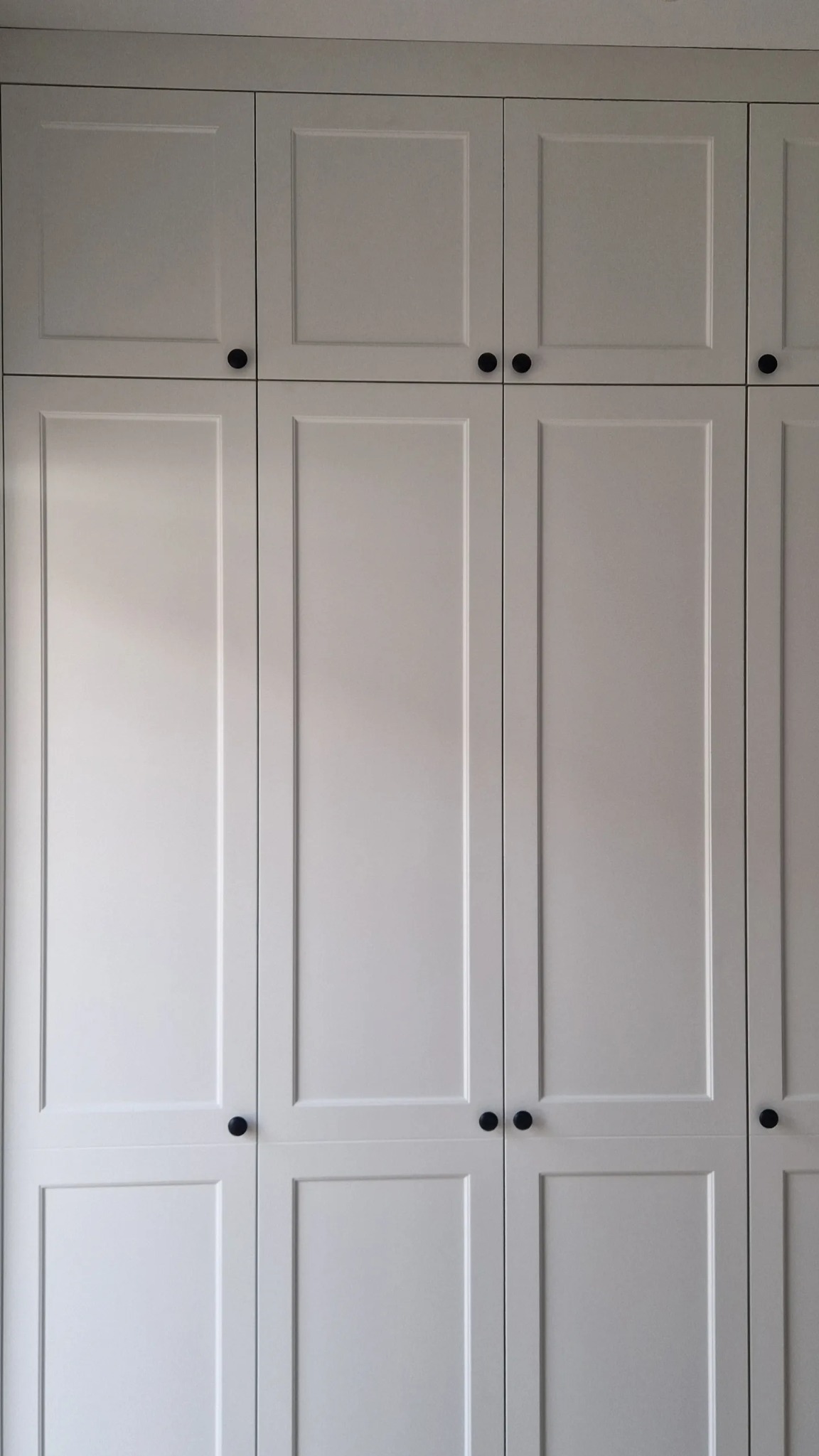 Biała szafa z frezowanymi frontami i czarnymi, okrągłymi uchwytami, widok na całą powierzchnię drzwi.