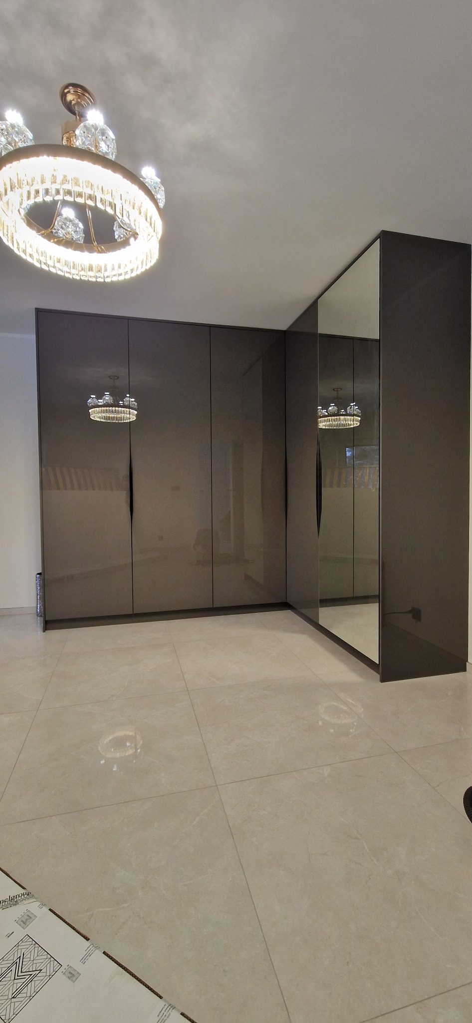 Nowoczesna, brązowa szafa wnękowa z lustrzanymi drzwiami, oświetlona kryształowym żyrandolem, zrealizowana w Stegnie.