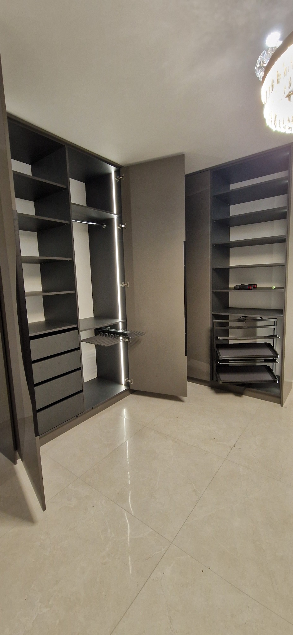 Nowoczesna szafa wnękowa z szarymi frontami, oświetleniem LED i wysuwanymi półkami na buty, ustawiona na jasnej, marmurkowej podłodze.