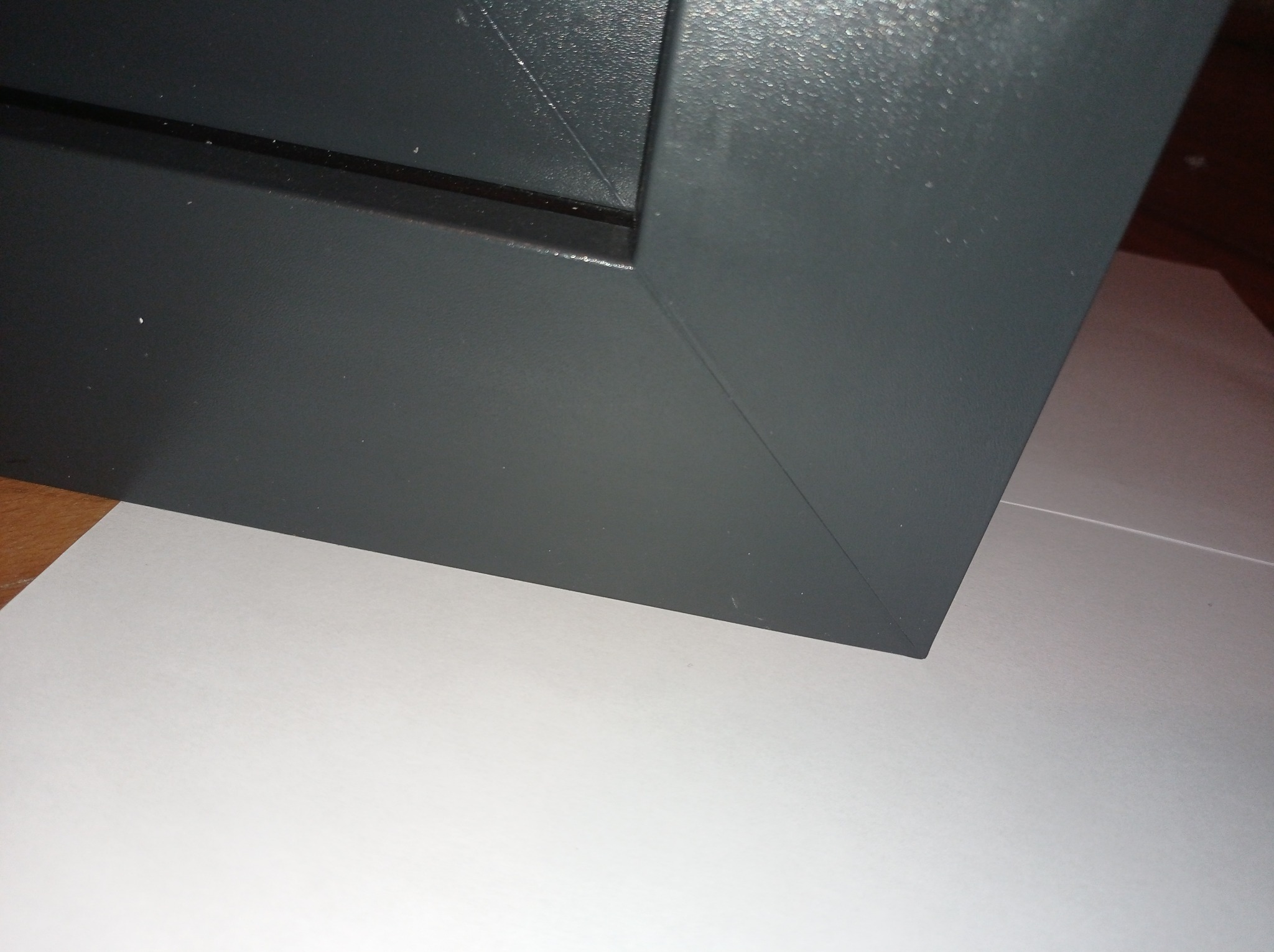 Szczegółowe ujęcie narożnika szarej ramy okiennej lub drzwiowej w Mławie, widoczna faktura malowanej powierzchni i krawędź na białym tle.