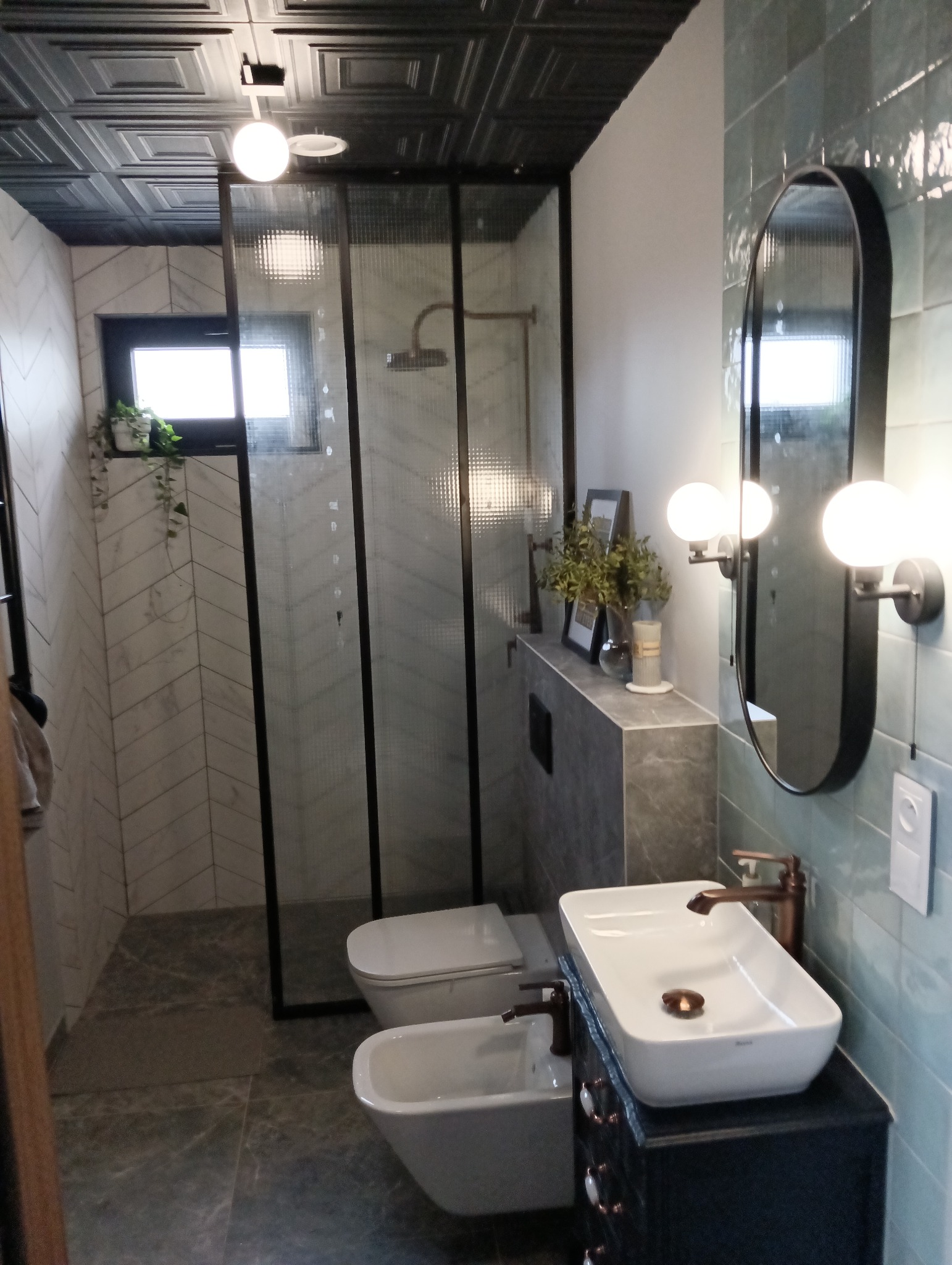 Nowoczesna łazienka z kabiną prysznicową typu walk-in z deszczownicą, umywalką nablatową na szafce z ciemnego drewna, bidetem i toaletą w zabudowie. Na ścianach płytki w odcieniach szarości...