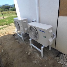 ARKEN - Dwie jednostki zewnętrzne klimatyzacji Panasonic, model Etherea, zamontowane na metalowych stojakach przy ścianie budynku z widocznymi przewodami chłodniczymi.