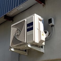 ARKEN - Jednostka zewnętrza klimatyzatora Haier Revive Plus zamocowanaa na podstawach na tyle kwiaciarni.