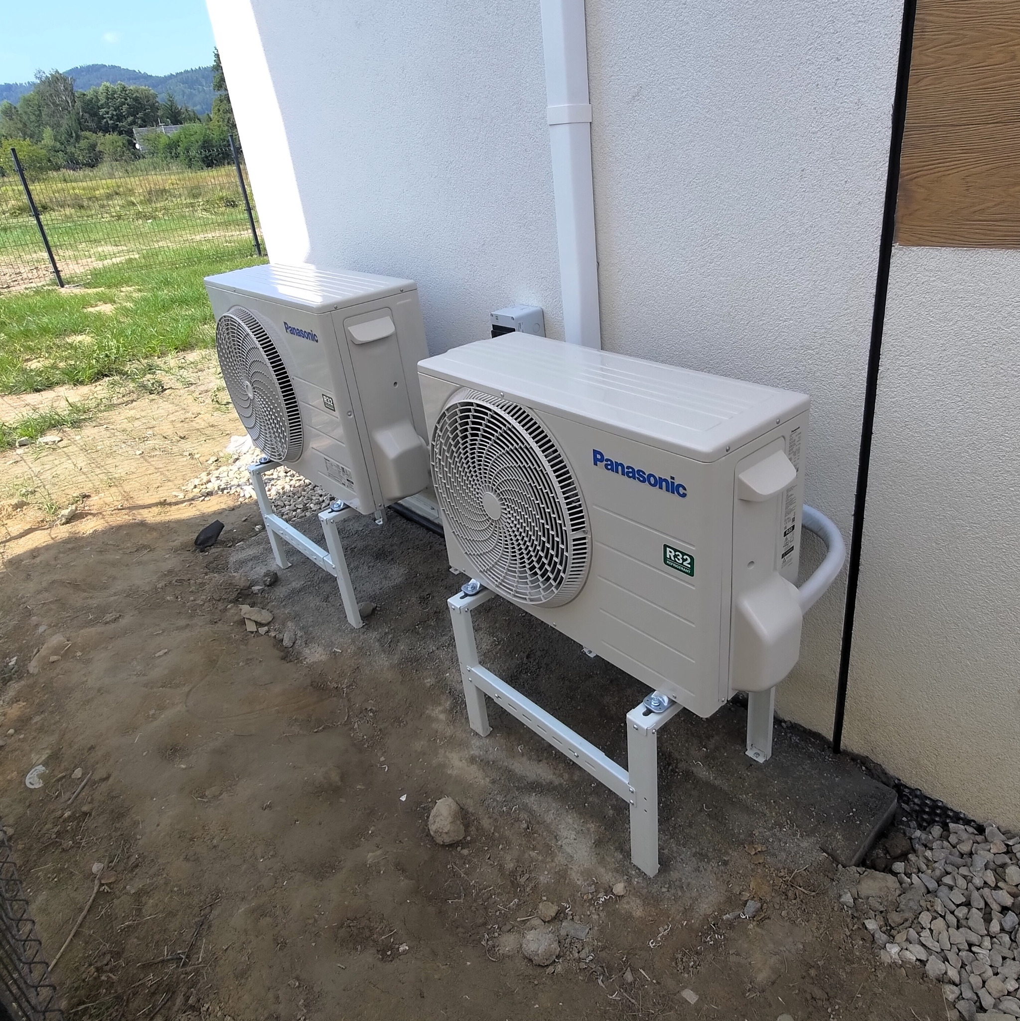 Dwie jednostki zewnętrzne klimatyzacji Panasonic, model Etherea, zamontowane na metalowych stojakach przy ścianie budynku z widocznymi przewodami chłodniczymi.