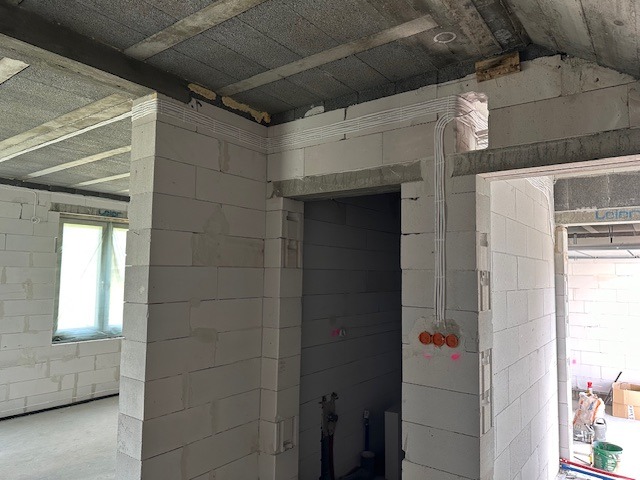 Instalacja elektryczna w surowym wnętrzu budynku w Starogardzie Gdańskim, widoczne kable prowadzone po ścianach z bloczków betonowych i przygotowane otwory pod gniazdka.