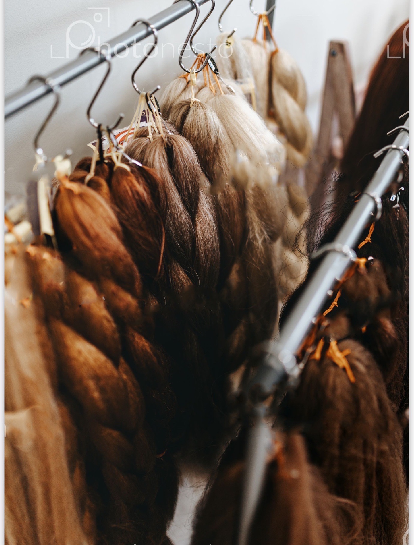 Różne odcienie warkoczy doczepianych, zawieszone na metalowym wieszaku w pracowni.