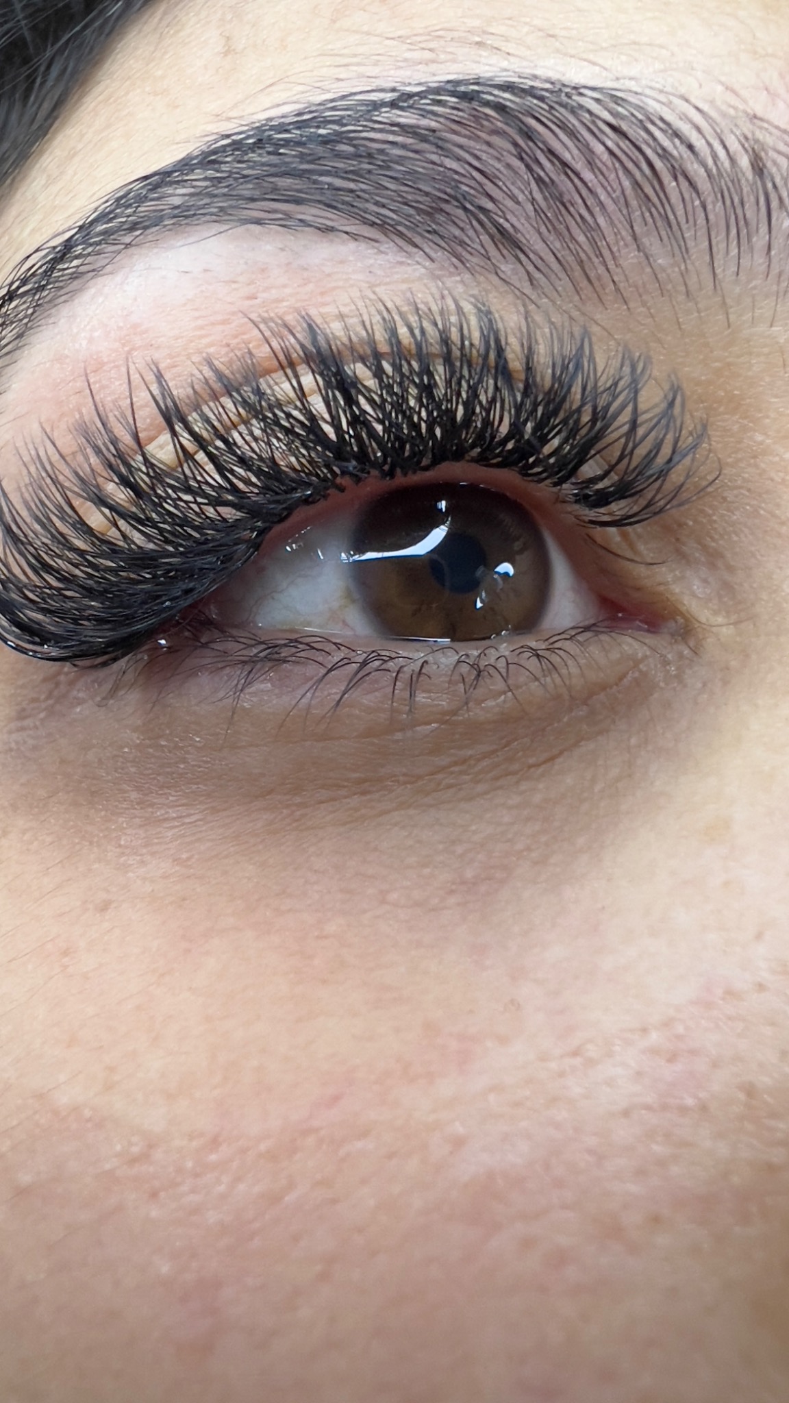 Zbliżenie na oko z długimi, gęstymi, sztucznymi rzęsami, brązowa tęczówka, widoczne drobne naczynka w białku oka.