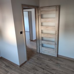 Uloo-instal - Zamknięte drzwi wewnętrzne z drewnianą ramą i przeszkleniami, widoczne na tle świeżo wykończonego wnętrza z panelami podłogowymi w odcieniach brązu i beżowe ściany w nowym budynku.