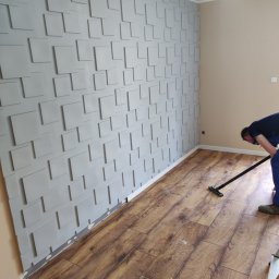 Uloo-instal - Montaż paneli podłogowych w pomieszczeniu z dekoracyjną ścianą z paneli 3D; widoczne narzędzie do czyszczenia podłogi i drabina