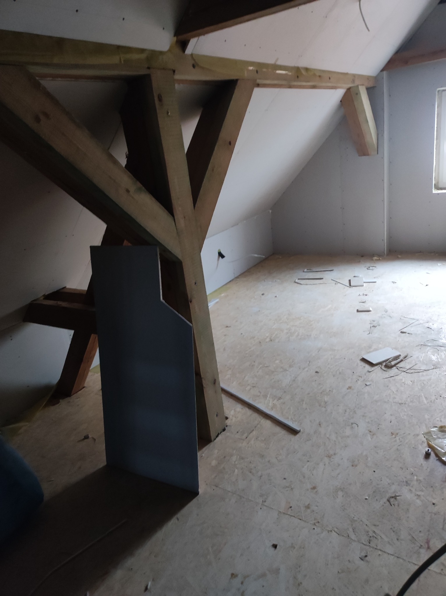 Poddasze w trakcie adaptacji: widoczne drewniane elementy konstrukcyjne, płyty karton-gips na ścianach i sufitach, surowa podłoga z płyt OSB. Etap prac wykończeniowych.