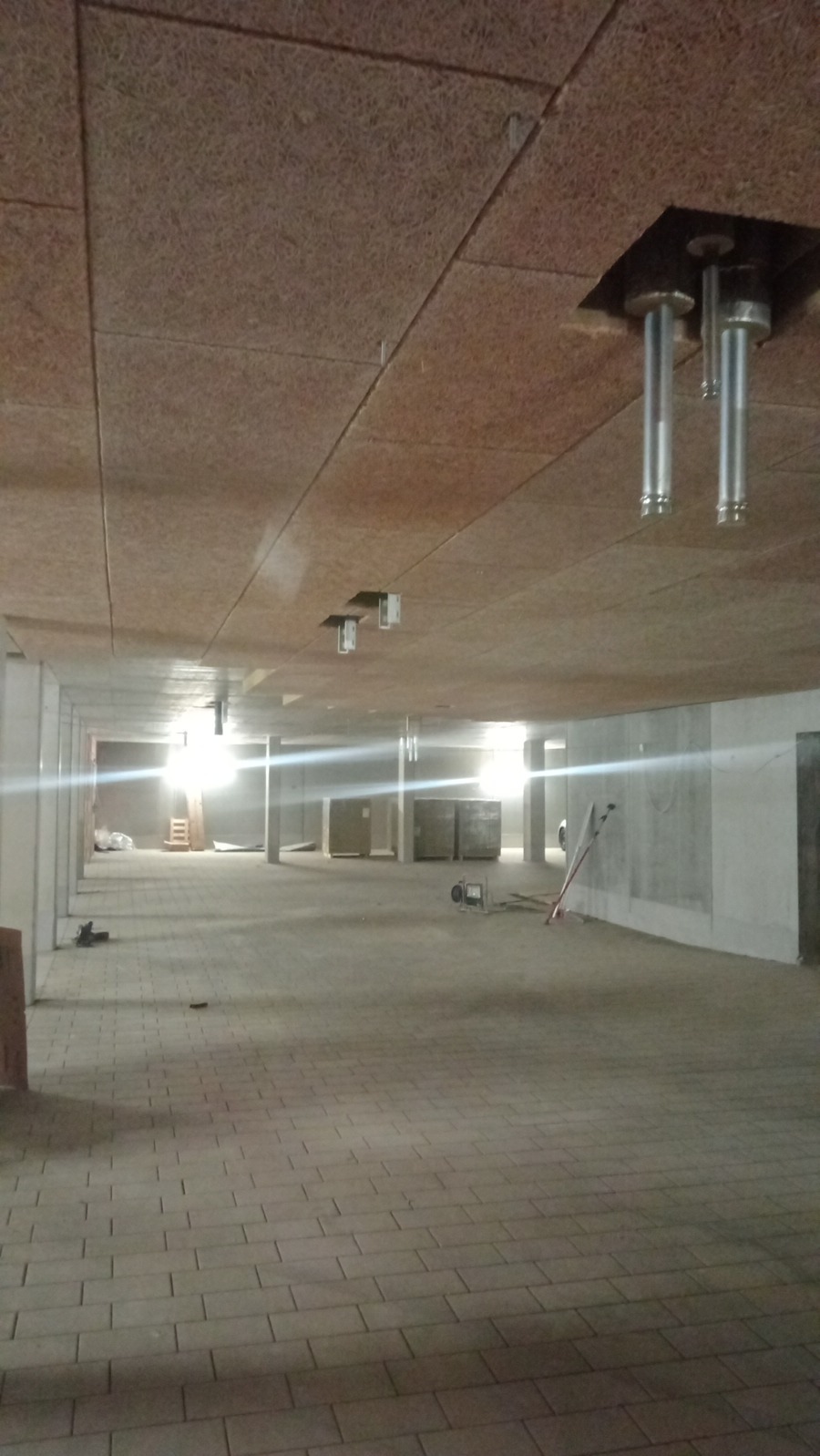 Wnętrze hali w trakcie prac wykończeniowych, widoczny sufit z paneli akustycznych, instalacje podwieszone, betonowa posadzka i ściany.