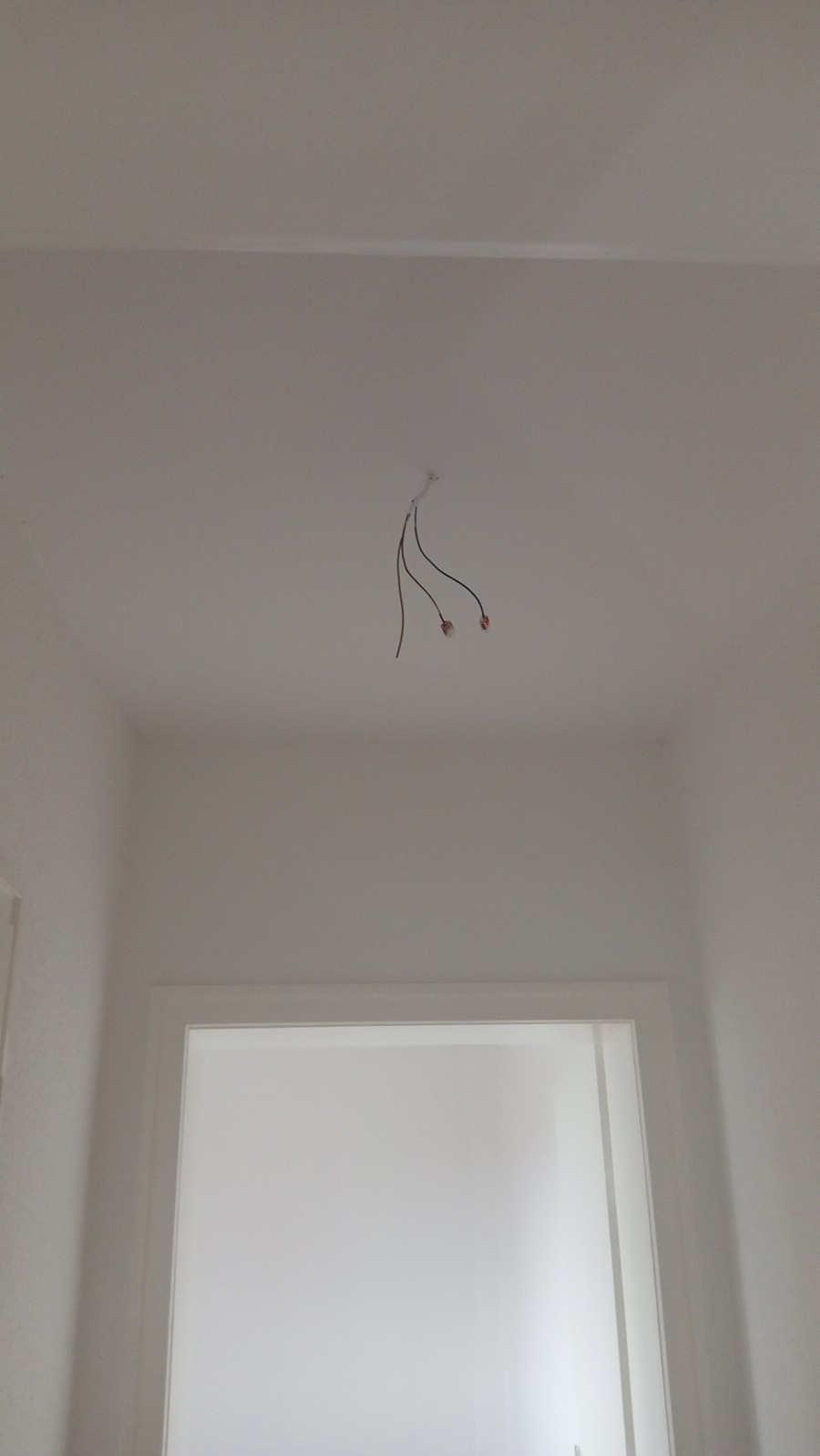 Białe wnętrze w trakcie malowania, widoczne wystające przewody z sufitu i rama drzwiowa