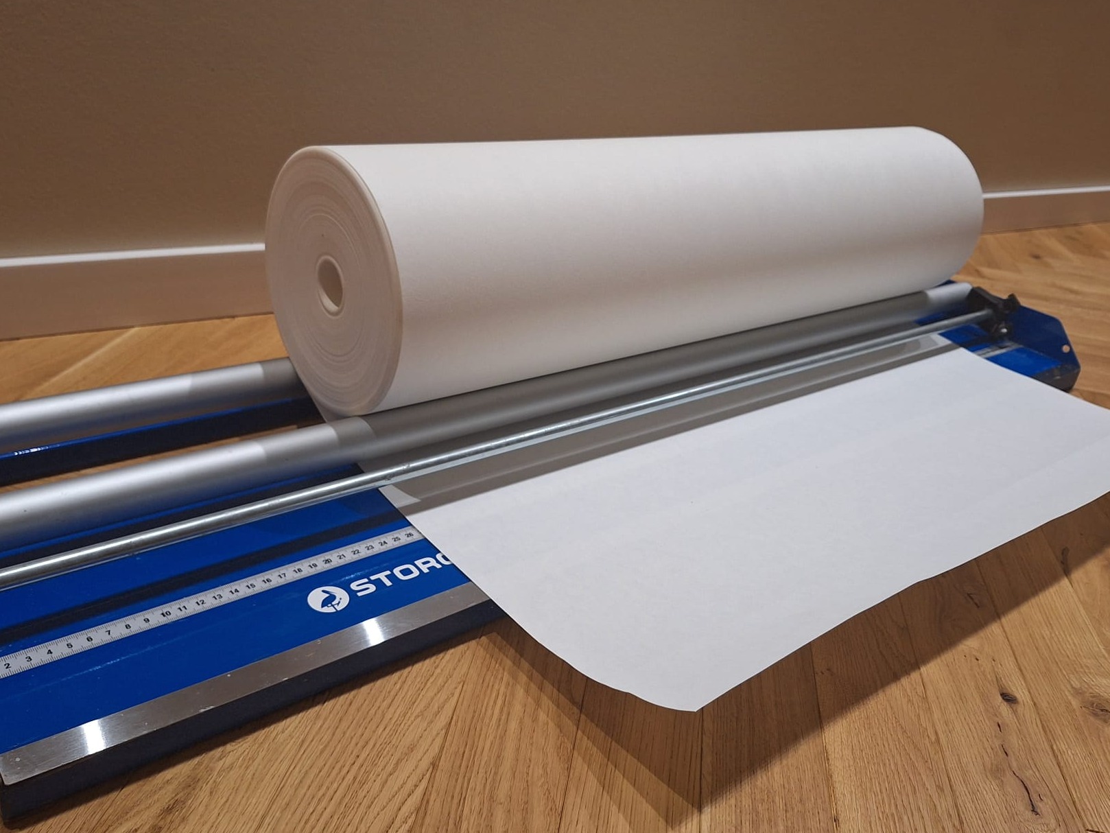 Rolka białego papieru na niebieskiej gilotynie do papieru marki Storck na drewnianej podłodze.