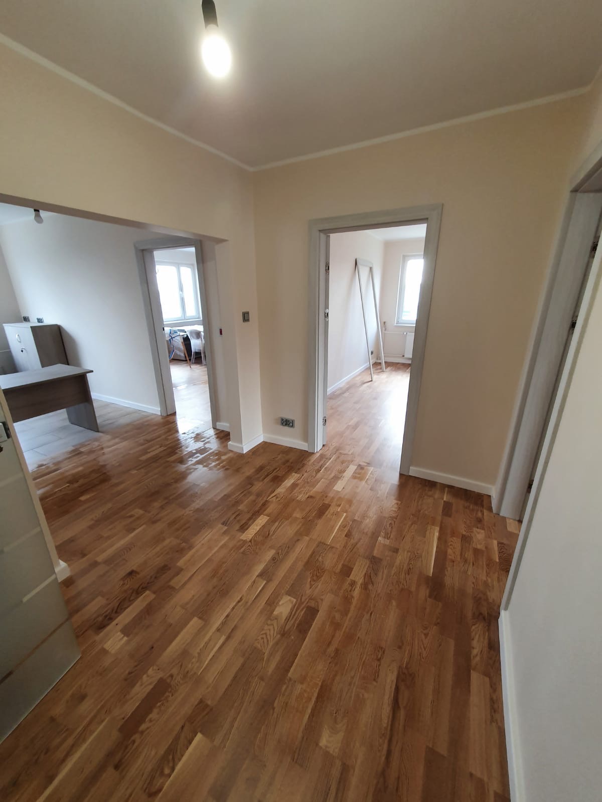 Wnętrze mieszkania po odświeżeniu, z parkietem ułożonym w jodełkę, kremowe ściany i szare ościeżnice drzwiowe, widok na dwa pokoje w głębi.