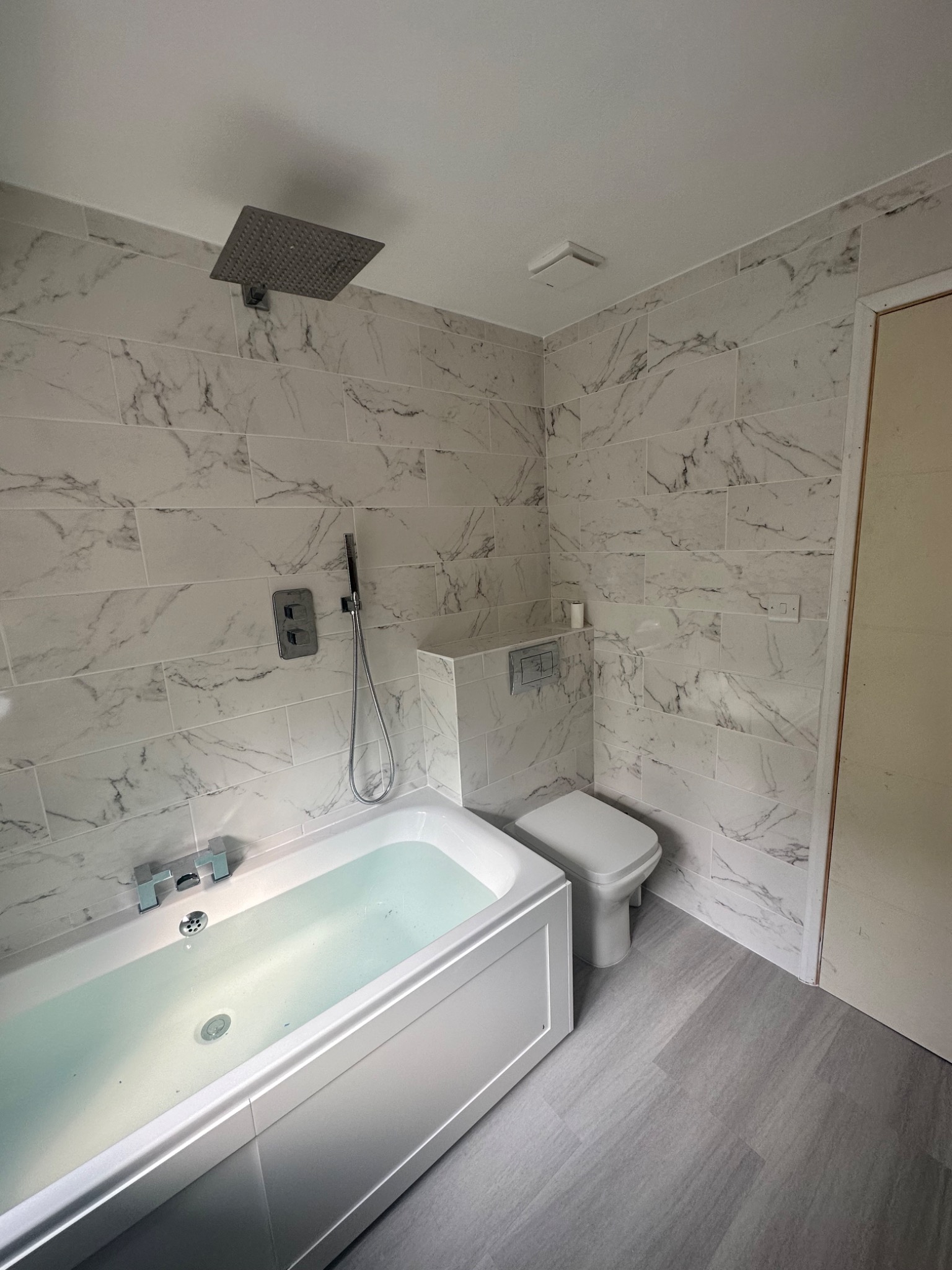 Wykończona łazienka z wanną wypełnioną wodą, toaletą i deszczownicą, wyłożona płytkami imitującymi marmur, widok z góry.