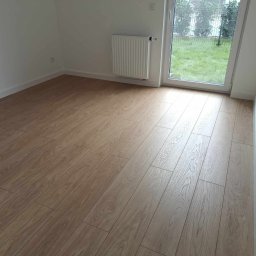 SERHII STARODUBTSEV AWANGARD - Jasne panele podłogowe ułożone w nowym pokoju z grzejnikiem i widokiem na ogród przez okno balkonowe.