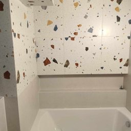 SERHII STARODUBTSEV AWANGARD - Wykończona łazienka z wanną, ściany i zabudowa wanny wyłożone płytkami imitującymi lastryko w odcieniach bieli, beżu, brązu i niebieskiego, widoczne zabezpieczenie folią na wannie.