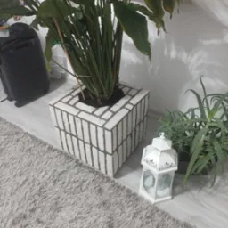 Dekoracyjny, murowany kwietnik z rośliną doniczkową, lampion i aloes na podłodze w Szczucinie. Kwietnik pomalowany na biało z szarą fugą.