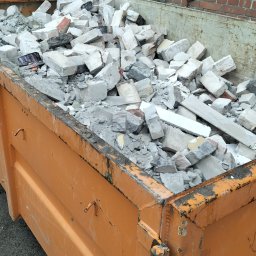 Ryn-Bud - Pomarańczowy kontener wypełniony gruzem budowlanym na tle ceglanego budynku z zamurowanymi oknami.