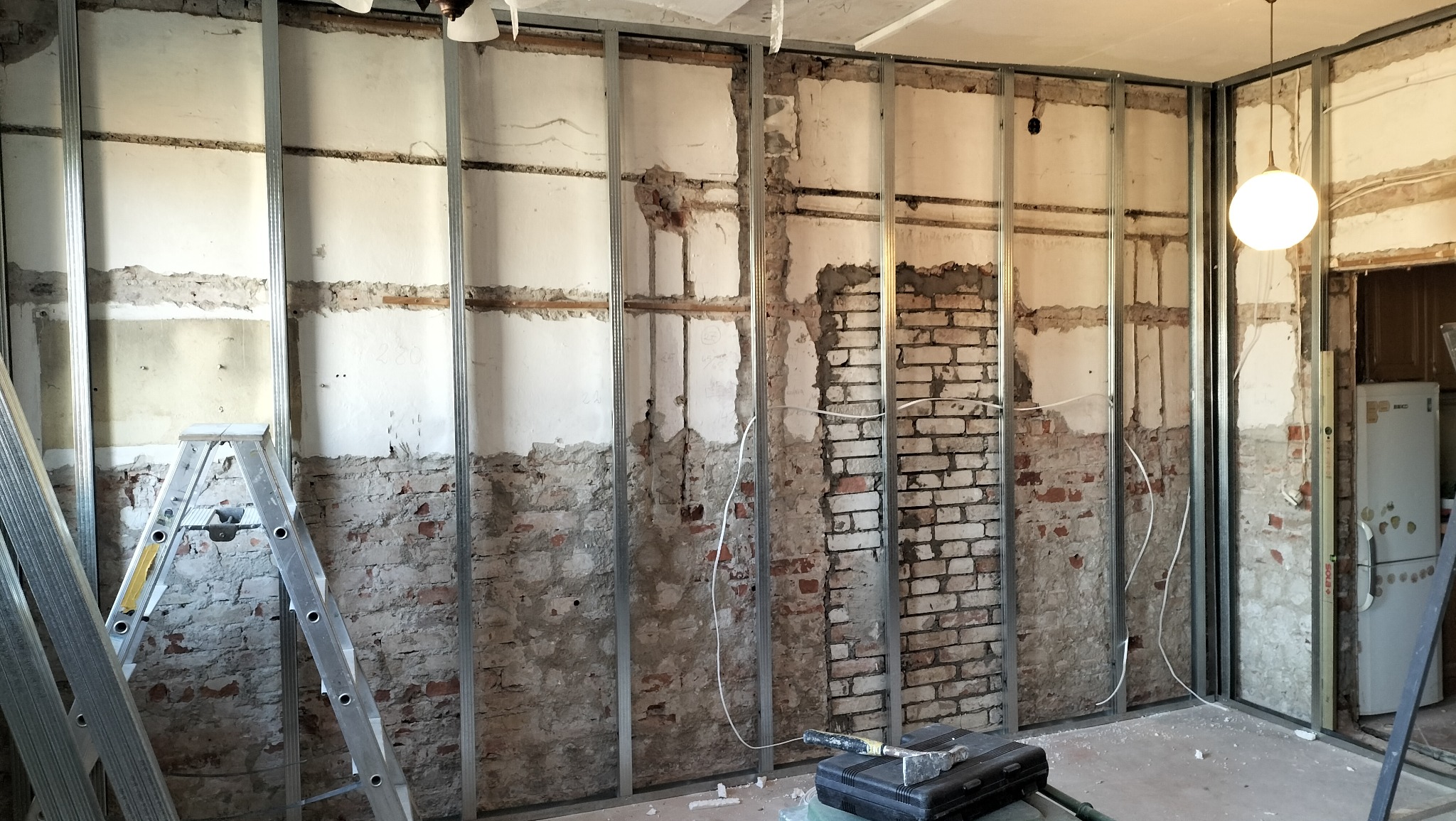 Remont pokoju: montaż metalowego stelażu pod płytę karton gips na tle odsłoniętej ceglanej ściany, widoczna drabina i narzędzia.