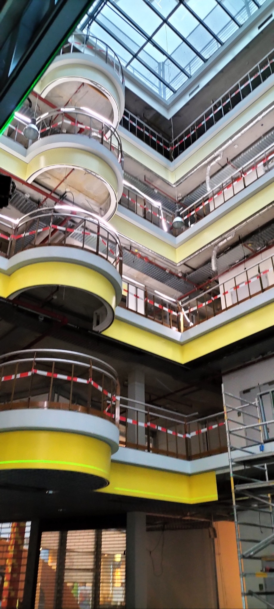 Wnętrze budynku w trakcie prac wykończeniowych z widocznymi balkonami, rusztowaniem i oszklonym dachem.