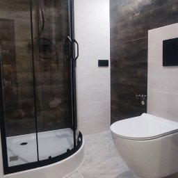 Kompleksowe wykończenia wnętrz - Nowoczesna łazienka z kabiną prysznicową typu walk-in z czarnymi profilami, podwieszaną toaletą i marmurową posadzką.