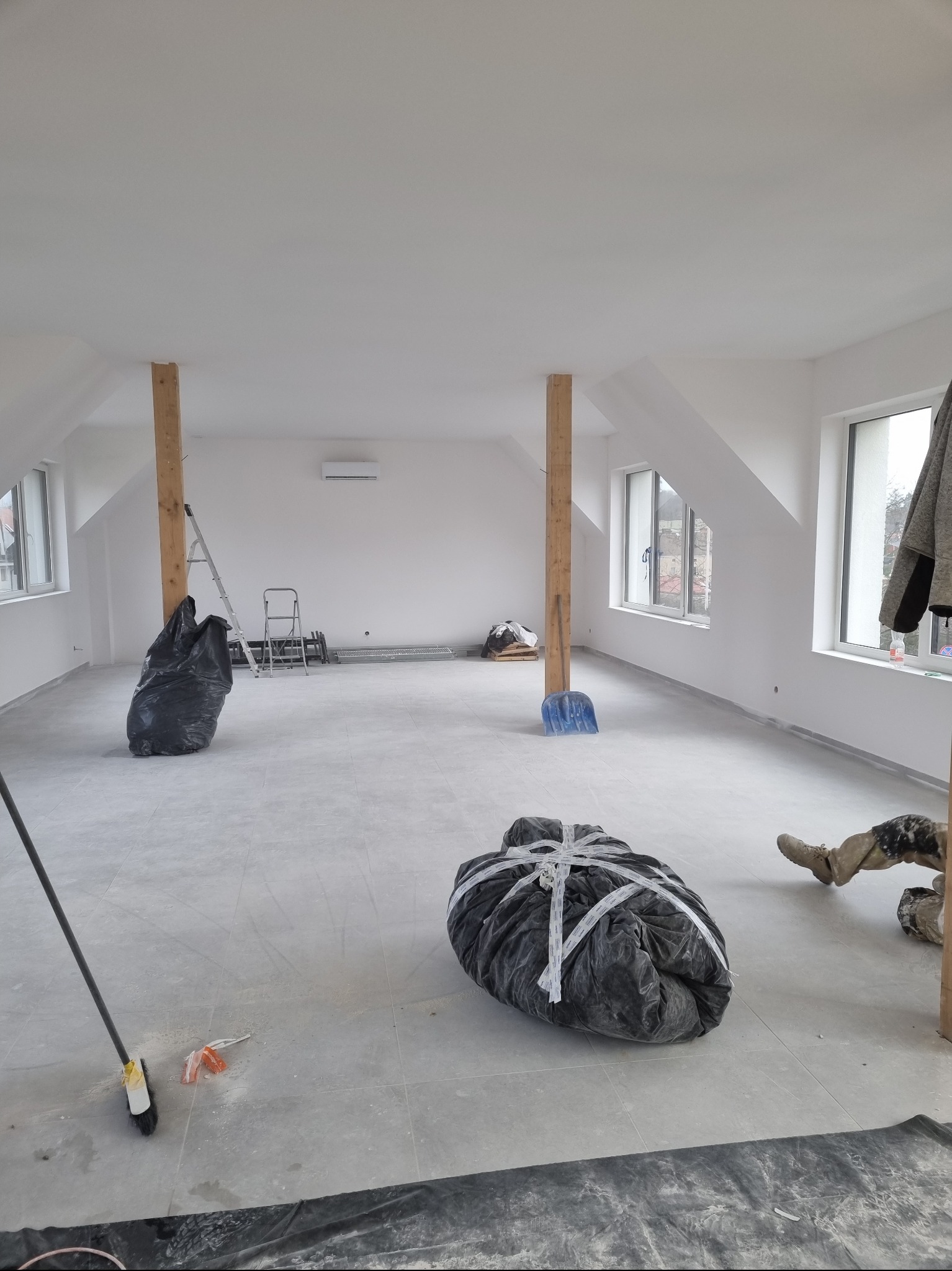 Poddasze po remoncie: świeżo pomalowane ściany na biało, dwa drewniane słupy, worki z gruzem, drabina, widoczne ślady prac wykończeniowych na podłodze.