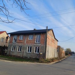 Michał Świerczyński - Dwupiętrowy dom w trakcie budowy z nowym, czarnym dachem, otoczony rusztowaniami, widoczny z perspektywy ulicy.