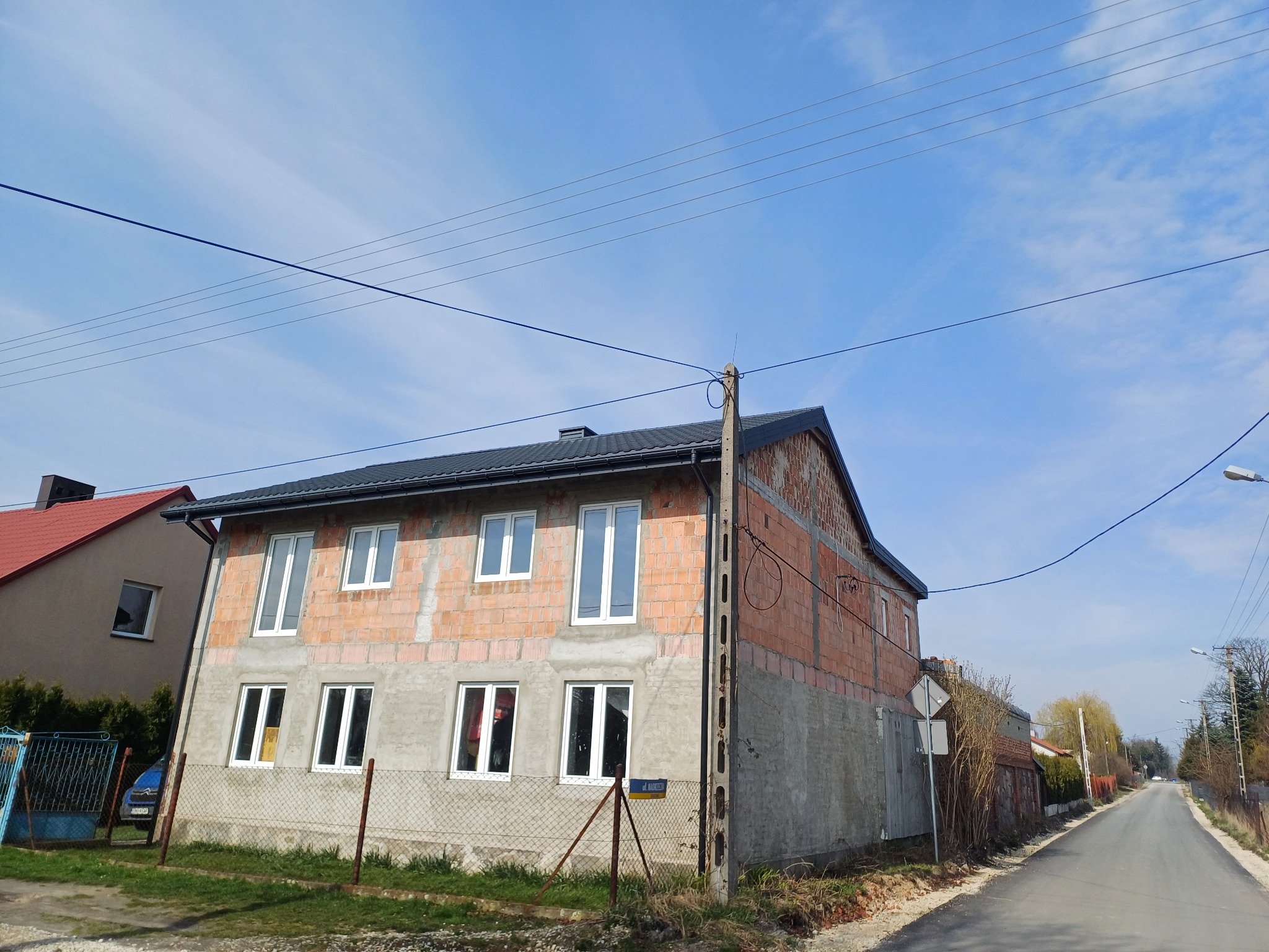 Budowa domu w Łodzi z nowym, ciemnym dachem i surowymi ścianami z cegły, widoczne okna i instalacja elektryczna na zewnątrz.